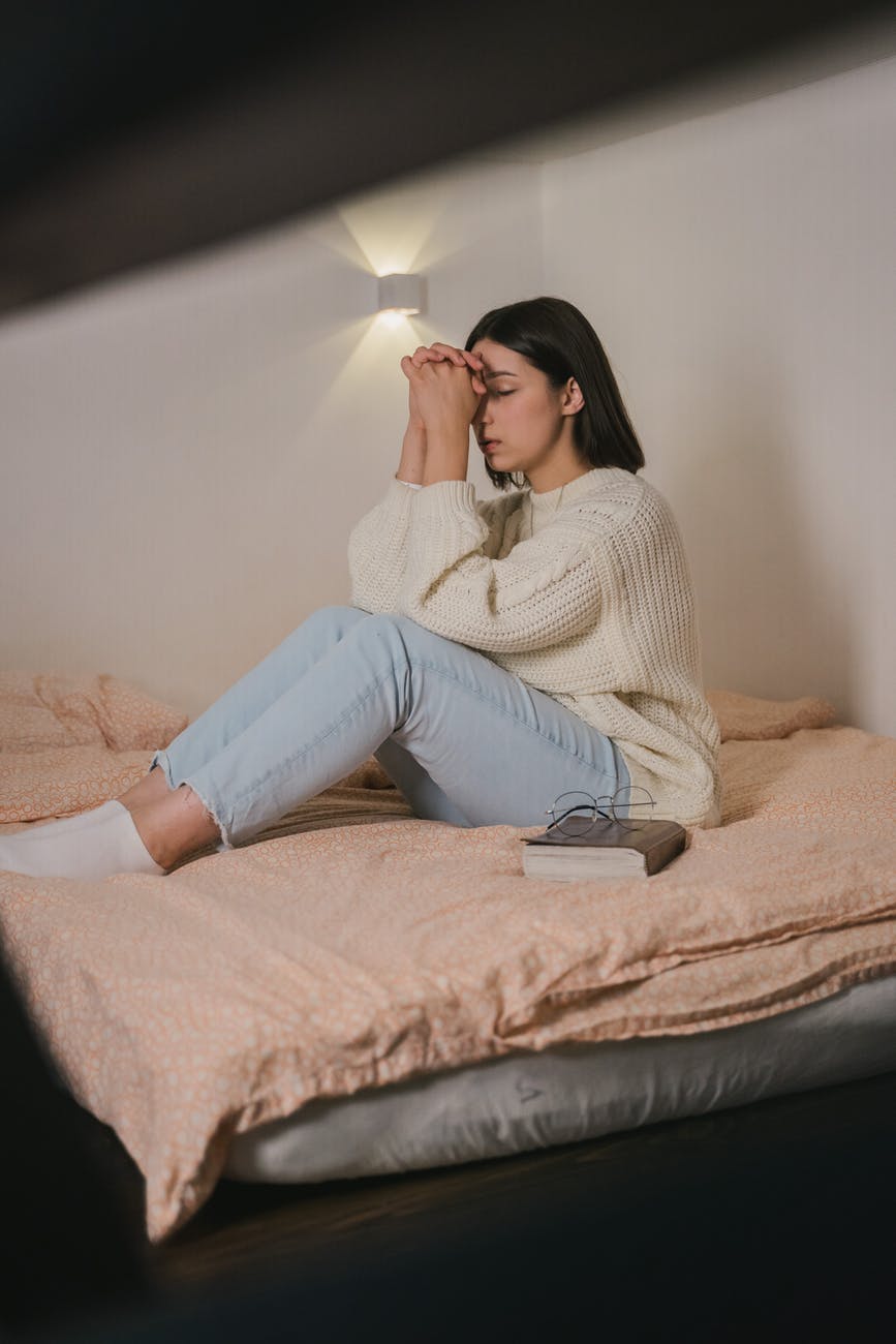 woman in white sweater and blue denim jeans sitting on bed